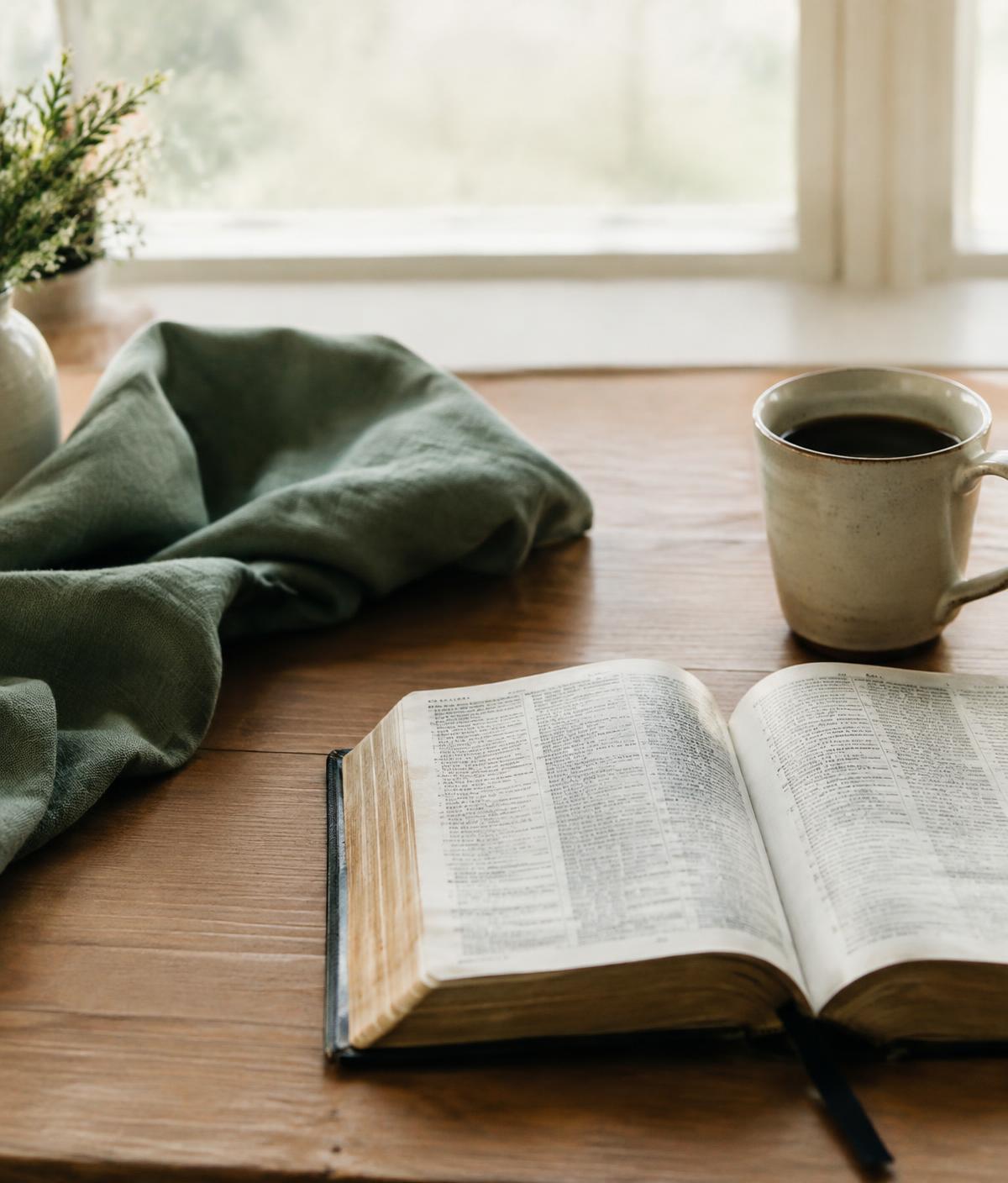 An open Bible and a cup of coffee on a wooden table by a window